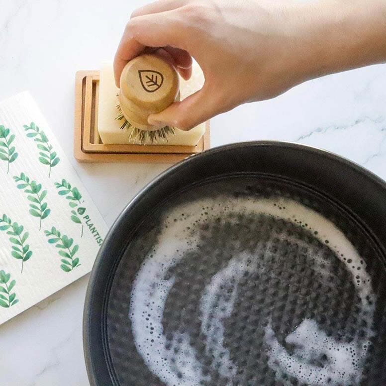 A person is lathering up a sisal scrubber on the solid dish soap, with a frying pan filled with foams next to it