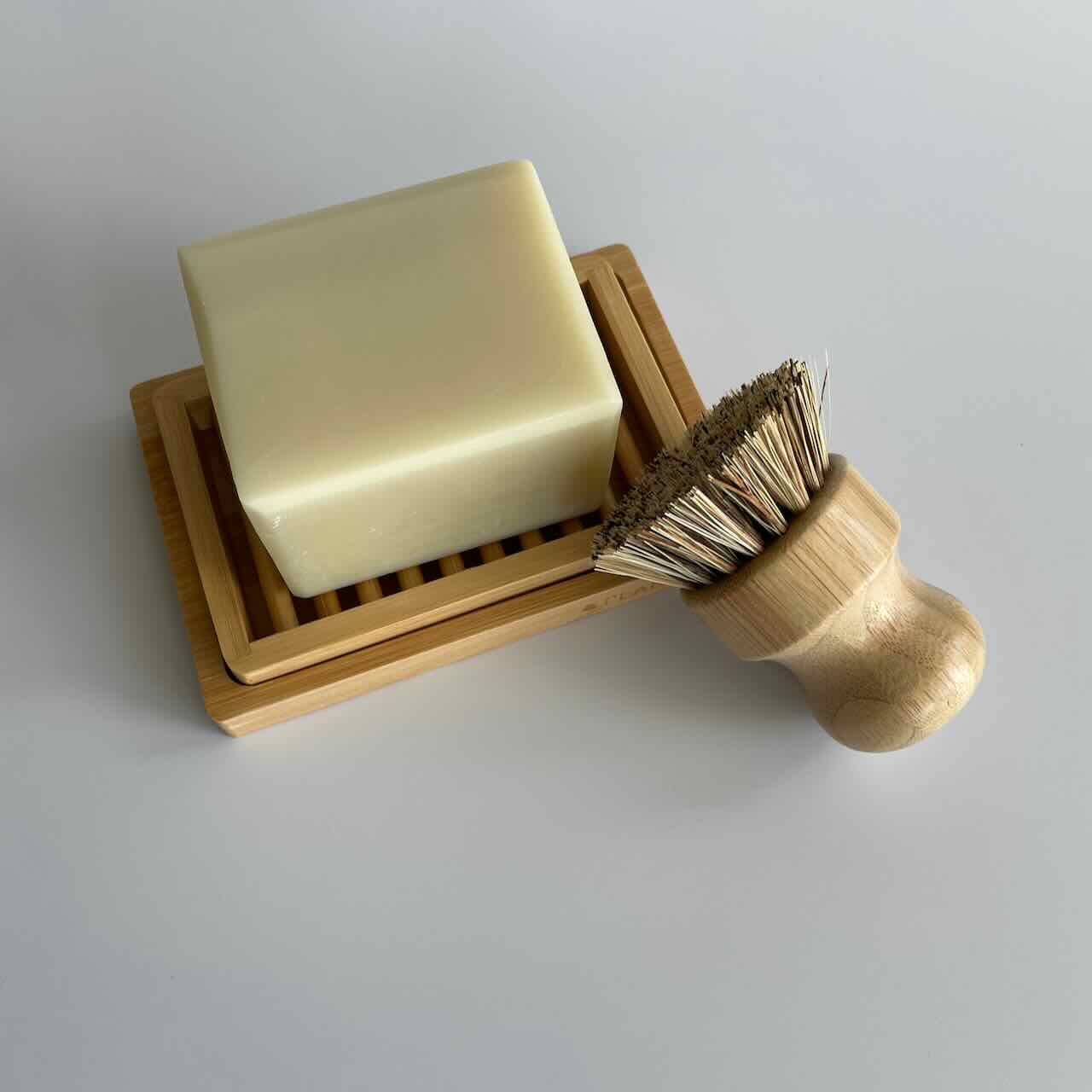 Solid dish soap resting on a bamboo soap dish, next to a pot scrubber made with sisal and bamboo.