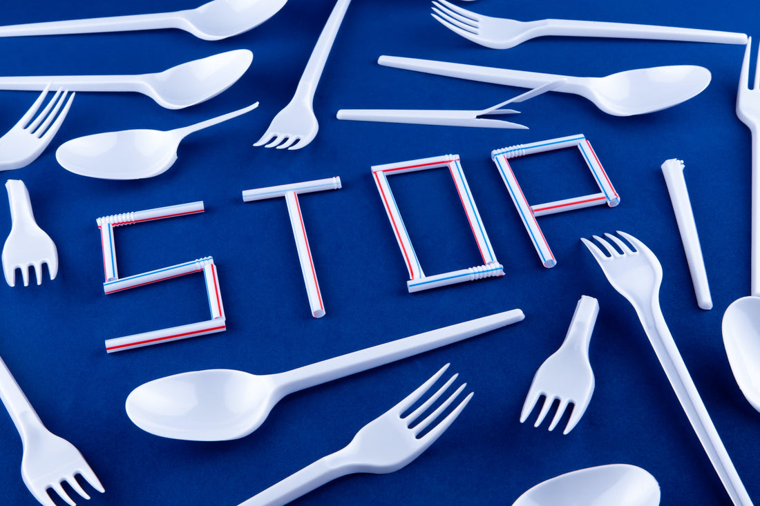 Flat lay of plastic spoons and forms on a blue surface, surrounding a white sign: "STOP" made up using plastic straws