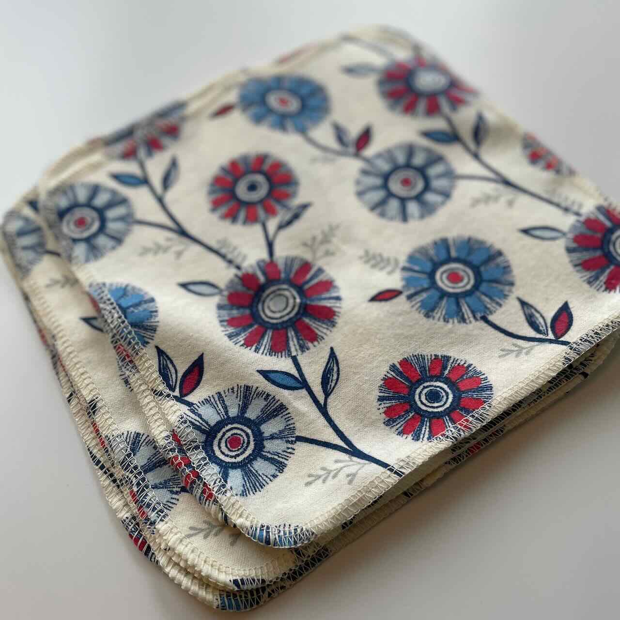 flat lay of a set of 10 reusable cloth wipes, with vibrant flower patterns printed on the fabric, side view.