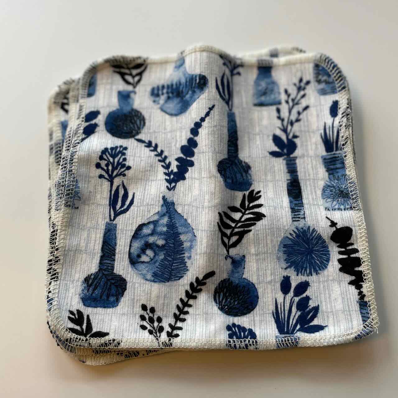 flat lay of a set of 10 reusable cloth wipes, with cool blue leaves and vases printed on the fabric, close up view