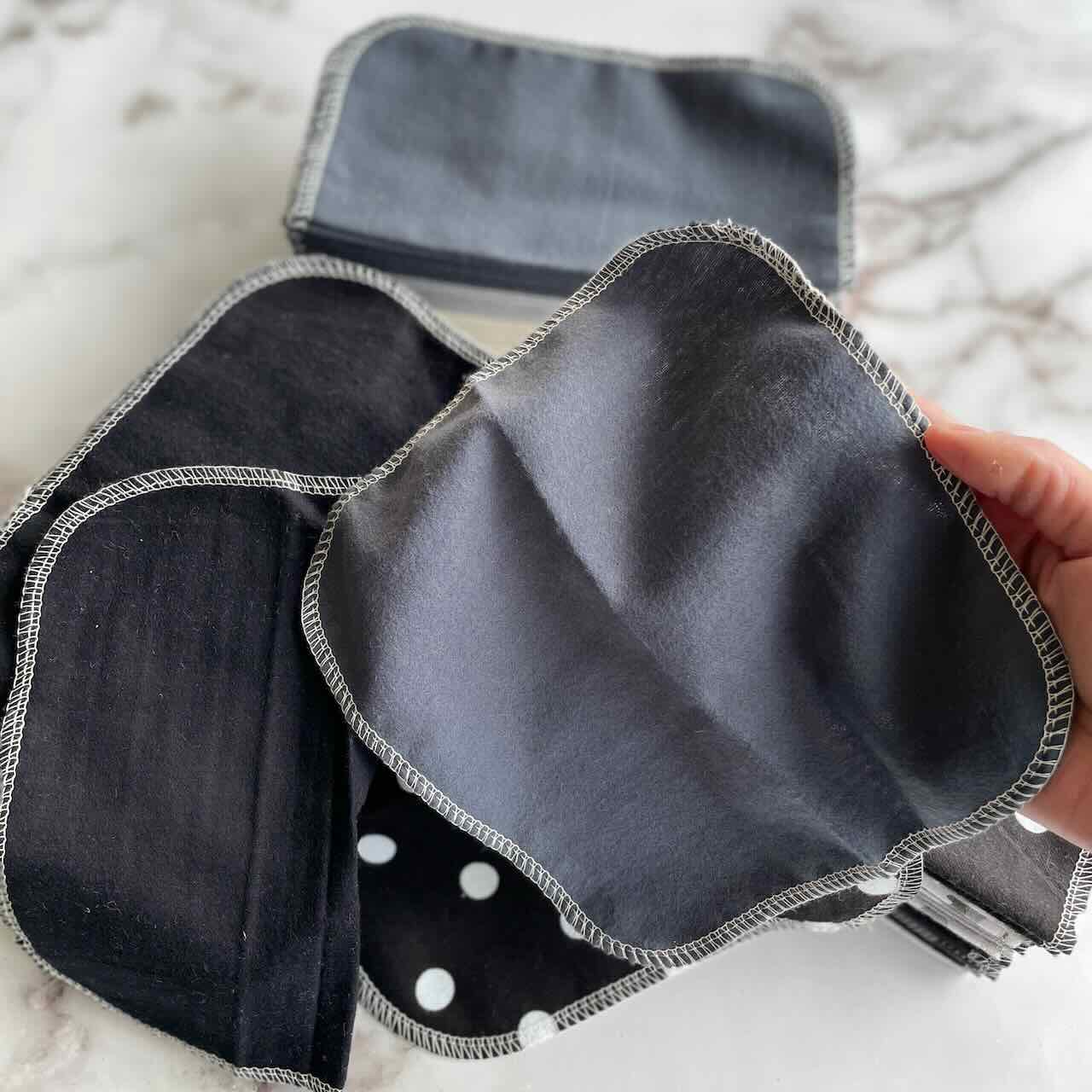A hand holding charcoal cheeks ahoy reusable cloth wipe with the rest of the cloth wipes at the background.