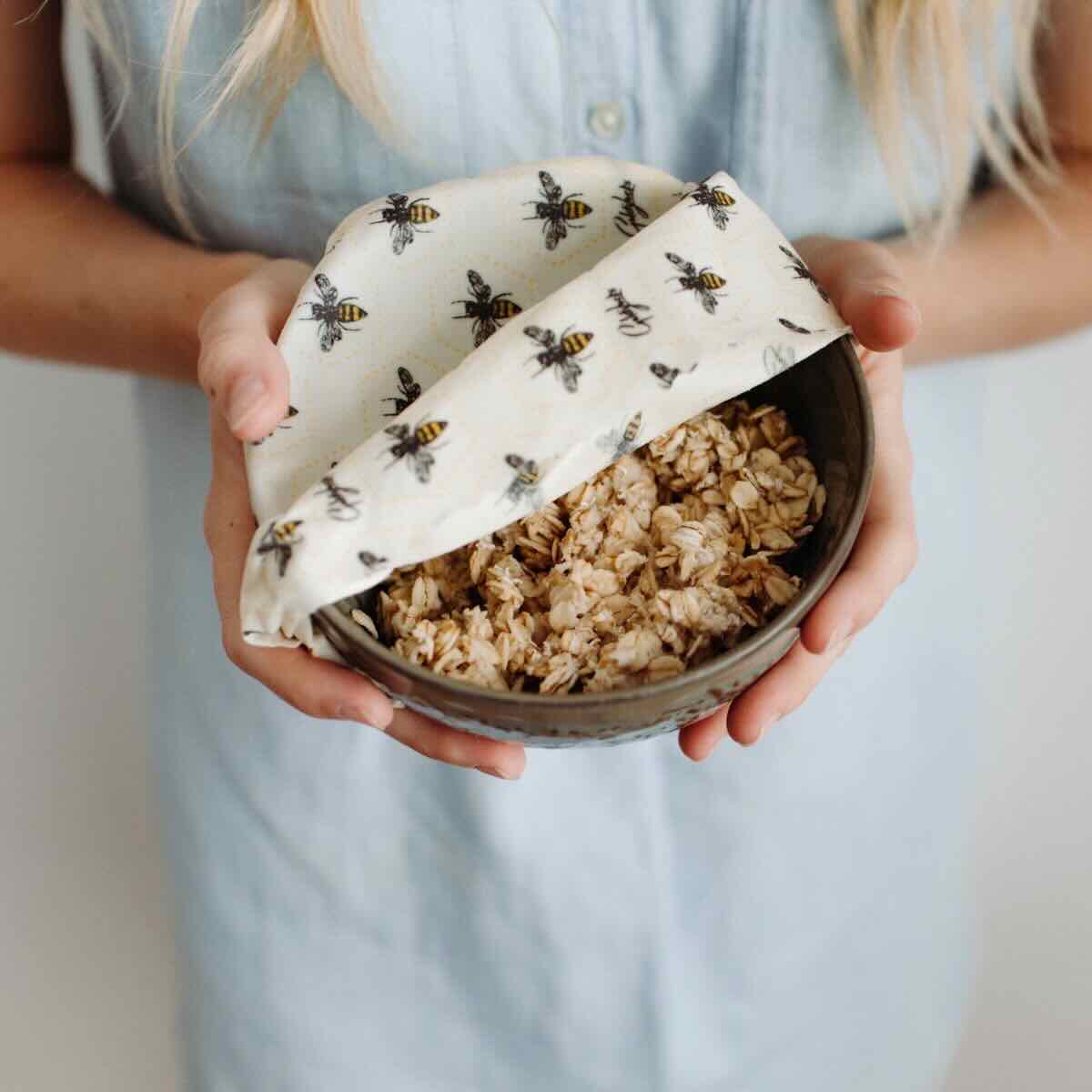 A woman holding a bowl with oats half covered by a Goldilocks bees themed beeswax wrap.
