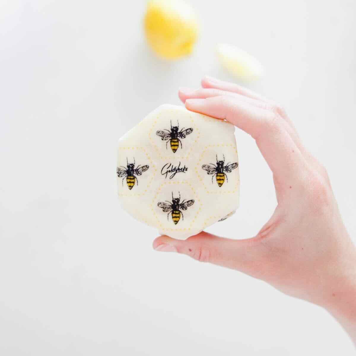 A woman holding half a lemon wrapped in Goldilocks bees themed beeswax wrap.