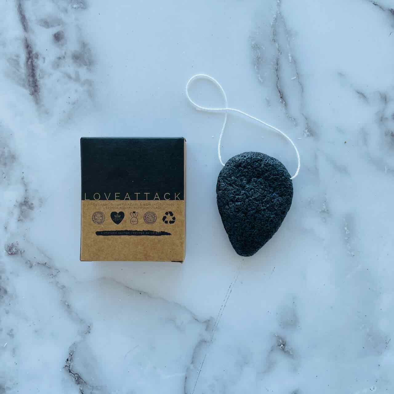 charcoal activated konjac sponge on a marble patterned table top next to its box.