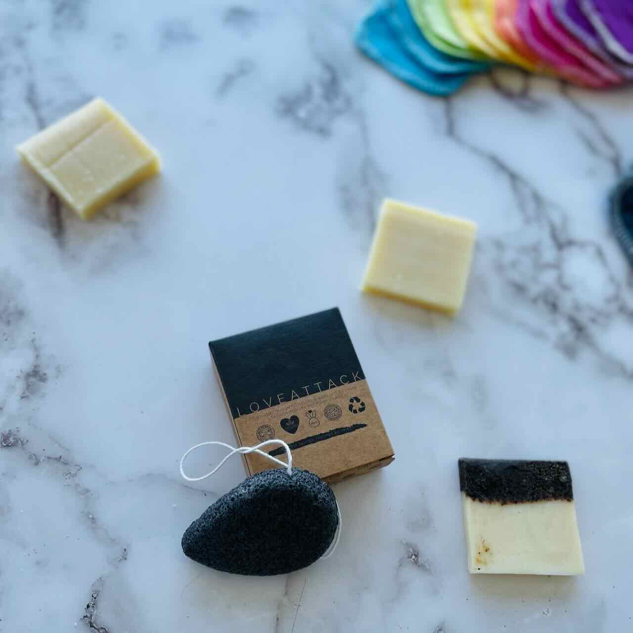 charcoal activated konjac sponge leaning on its box on a marble patterned table top with soaps scattered around it