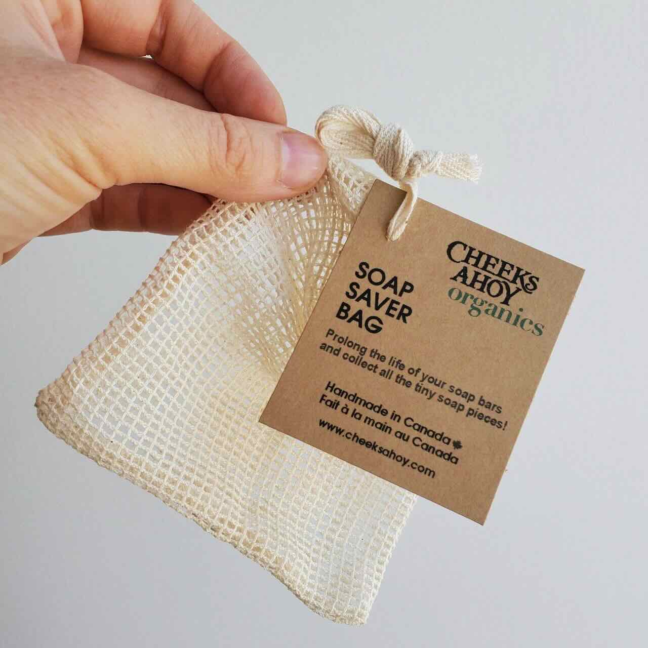Cheeks Ahoy Soap Saver Bag being held up on a finger tip, with label clearly shown: hand made in Canada, Organic