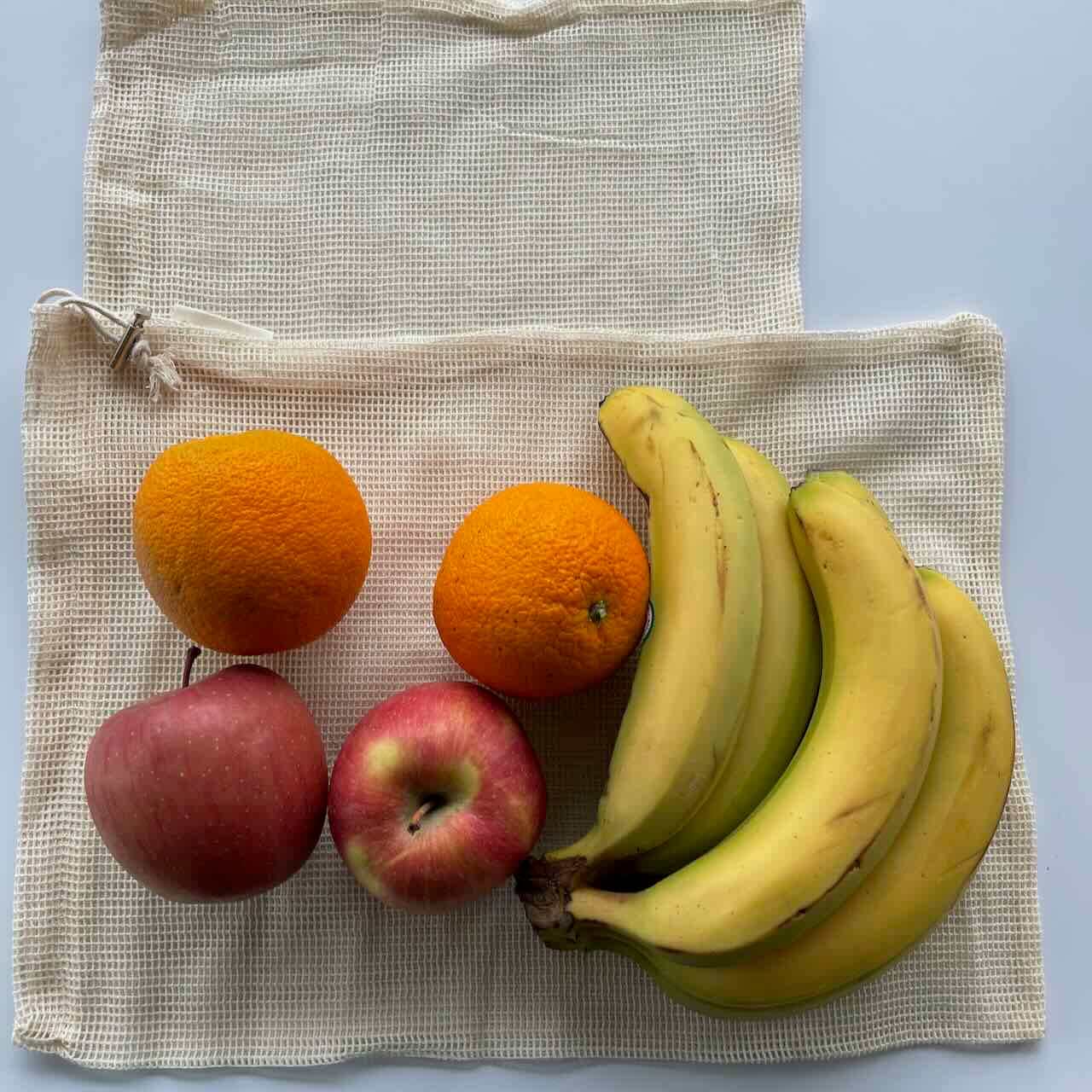 a bunch of bananas, two large oranges and two large apples on top of a large mesh bag,