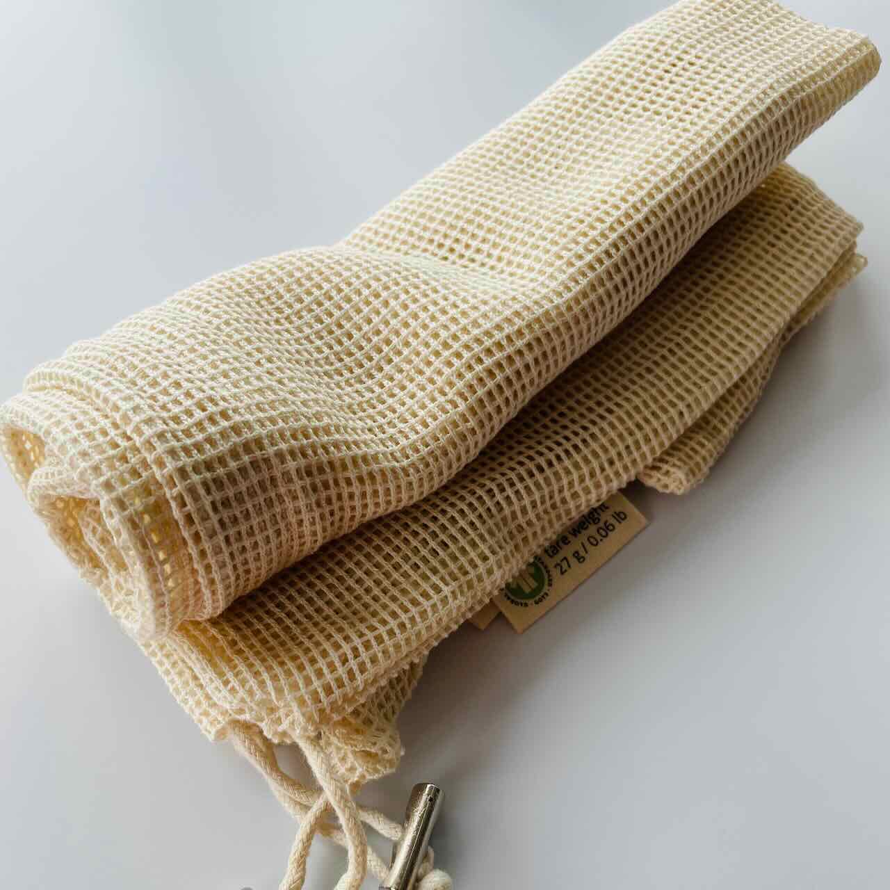 two reusable muslin produce bags folded up on a table top.