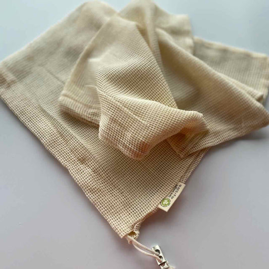 two reusable muslin produce bags laid on a table top.