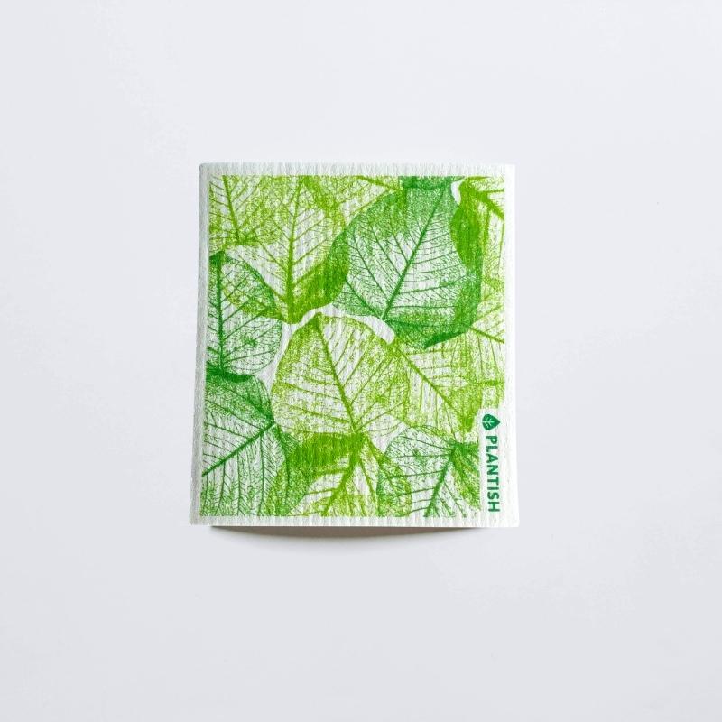 A green vessel patterned swedish dish cloth made by Plantish on a white table top.