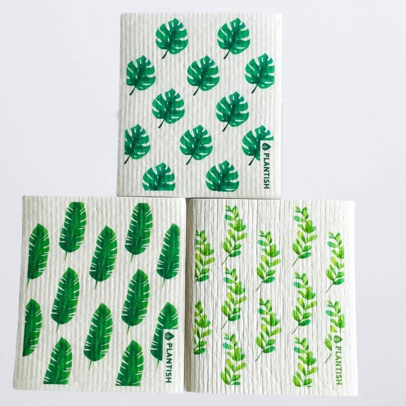 set of 3 swedish dish cloths on a white table top. The patterns are inspired by green leaves: bird of paradise,  swiss cheese and eucalyptus.