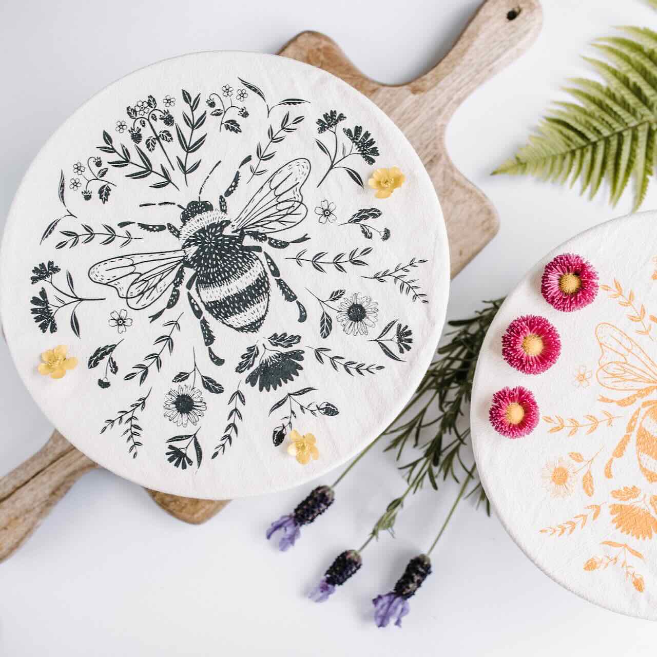 flat lay of two bowls covered by a charcoal fabric bowl cover and a yellow fabric bowl cover, with lavenders as decoration.