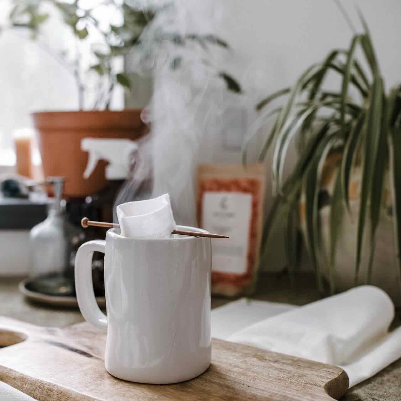 A reusable tea bag with balancing stick inside a white mug, brewing, as white smoke coming out of the mug.