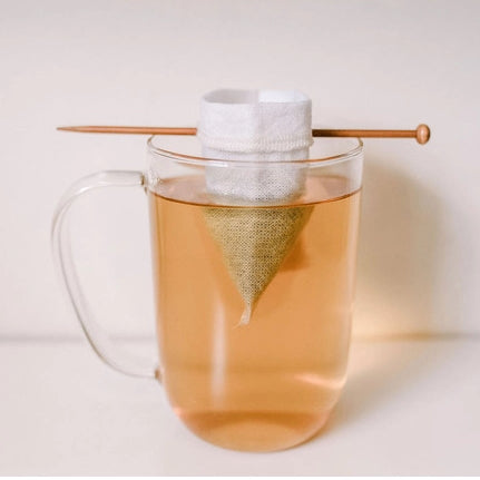 A product shot of tea brewing inside a glass tea cup, with balancing stick holding up the tea bag,